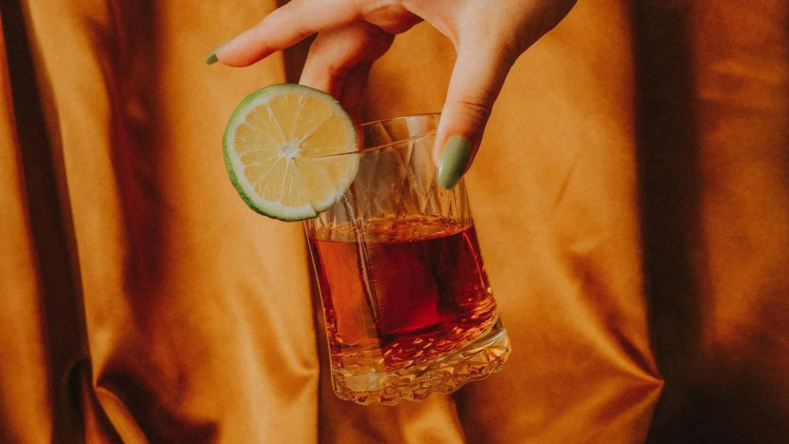 Une main tenant un Apéritif sans Alcool avec une tranche de citron vert dedans.