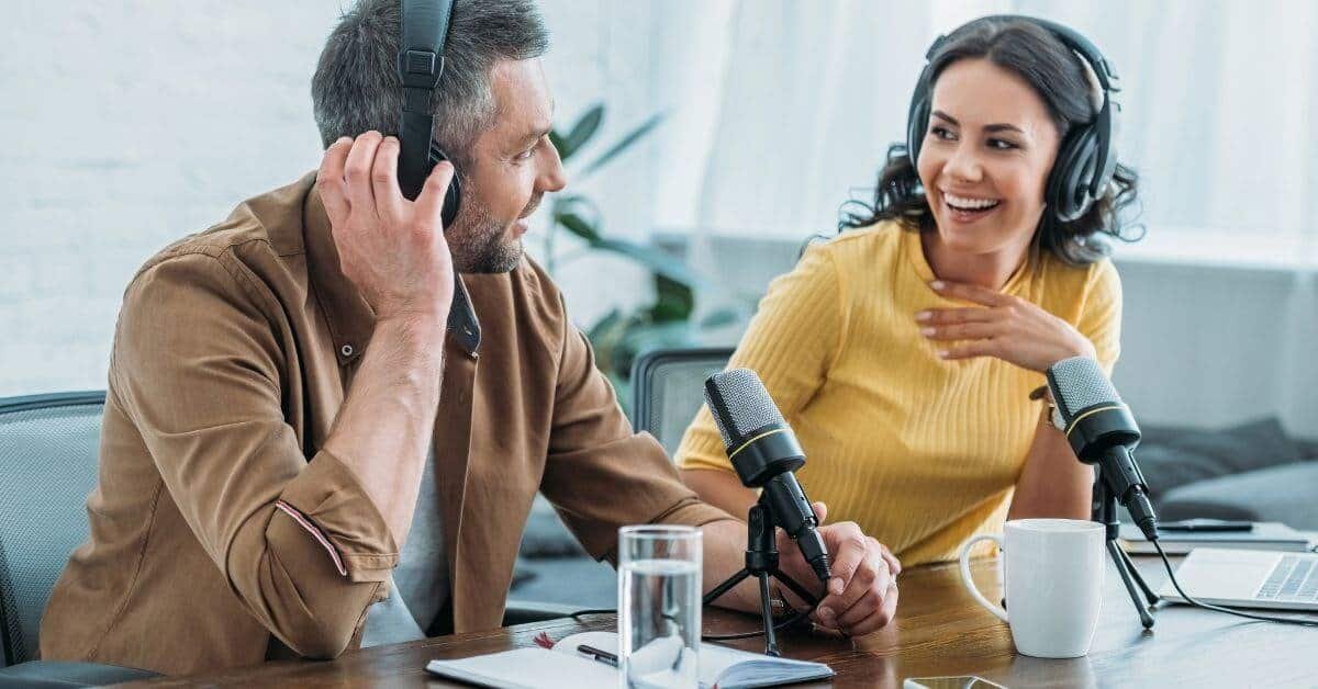 Un homme et une femme attablés avec des micros, enregistrent un podcast.