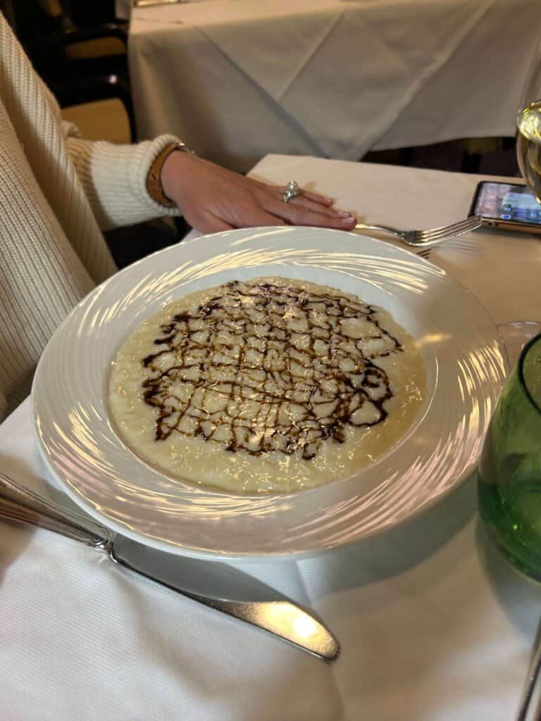 Une personne assise à une table à manger avec une assiette de risotto surmontée d'un motif de glaçage au vinaigre balsamique, profitant de son week-end à Milan.